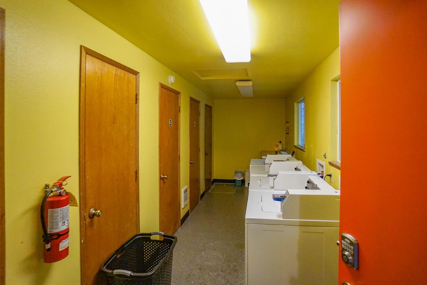 Laundry room with yellow walls, washing machines, doors, and a fire extinguisher.
