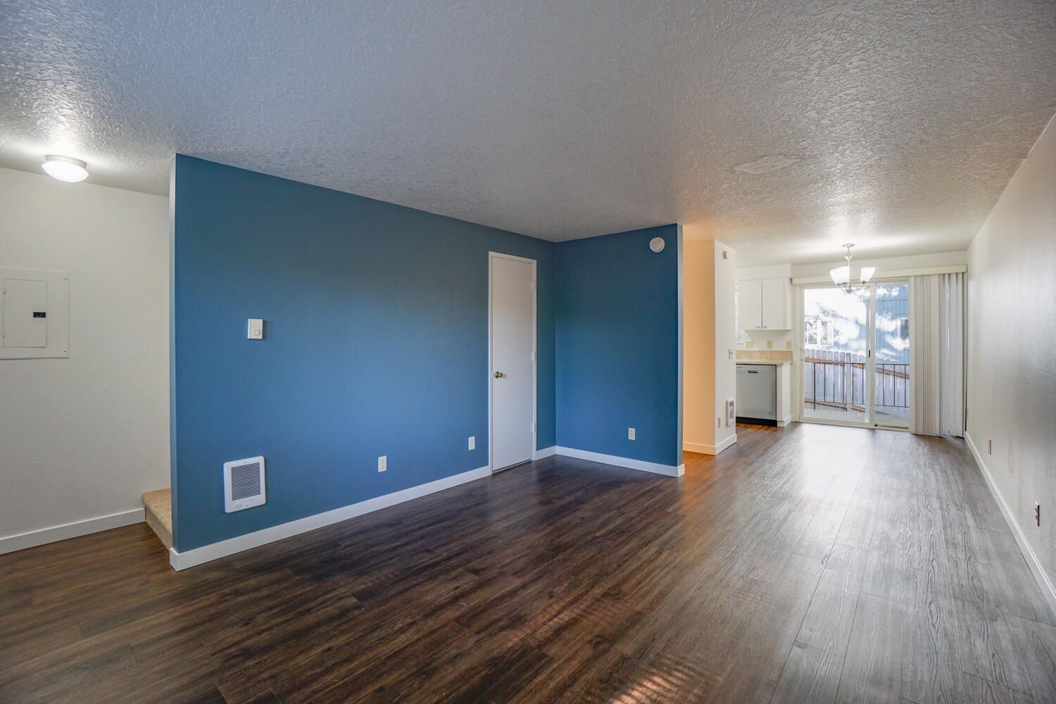 Living room with dark wood floor, blue accent wall, and white door leading to kitchen and balcony.