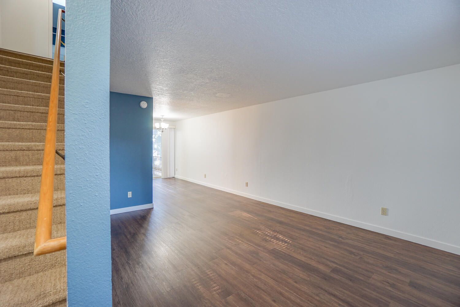 Interior view of a living space with a staircase. Features wood flooring, white walls, and a blue accent wall.