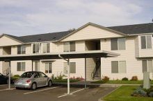 A car is parked under a canopy in front of a apartment building.