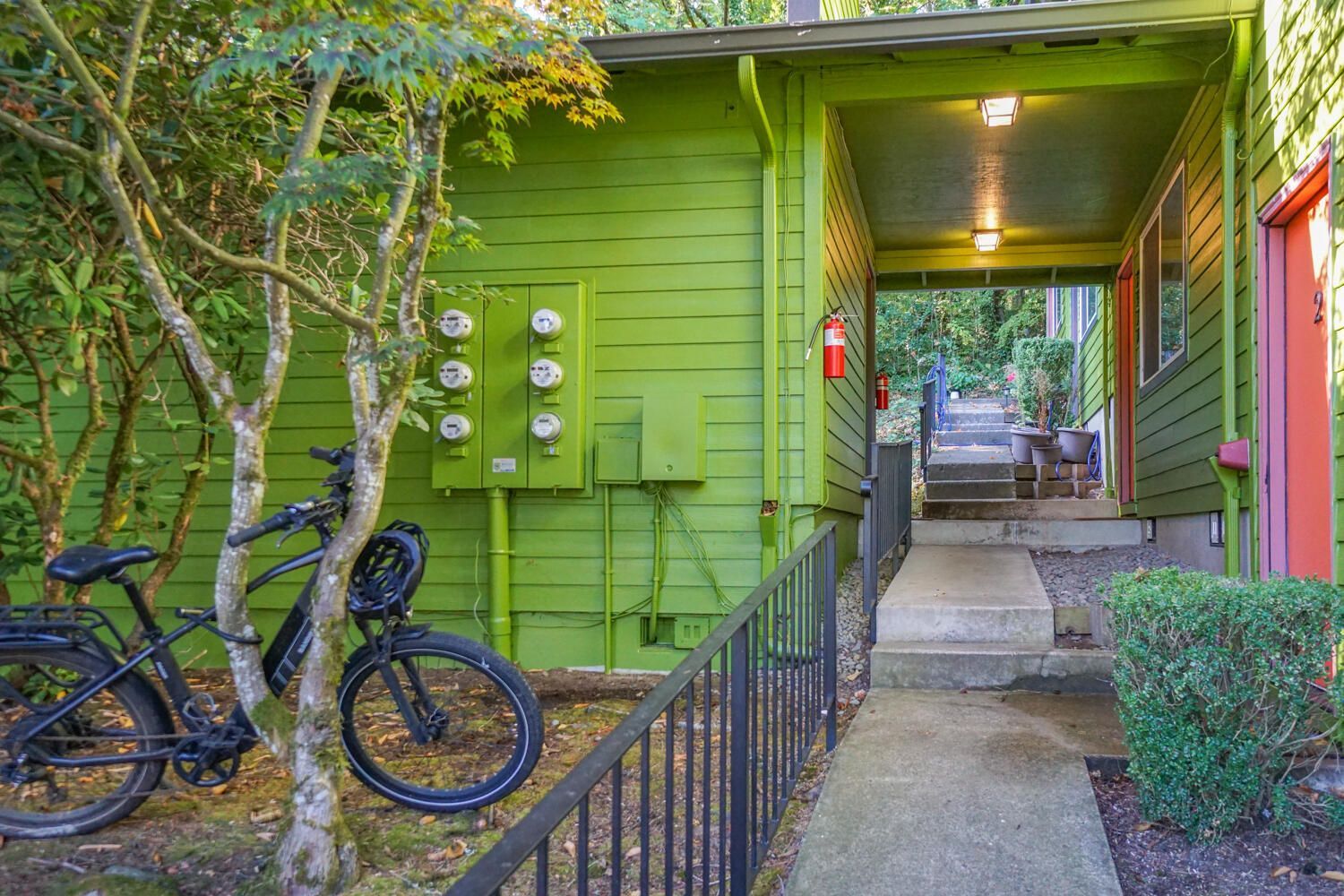 Green building entrance with bike, concrete path, stairs.
