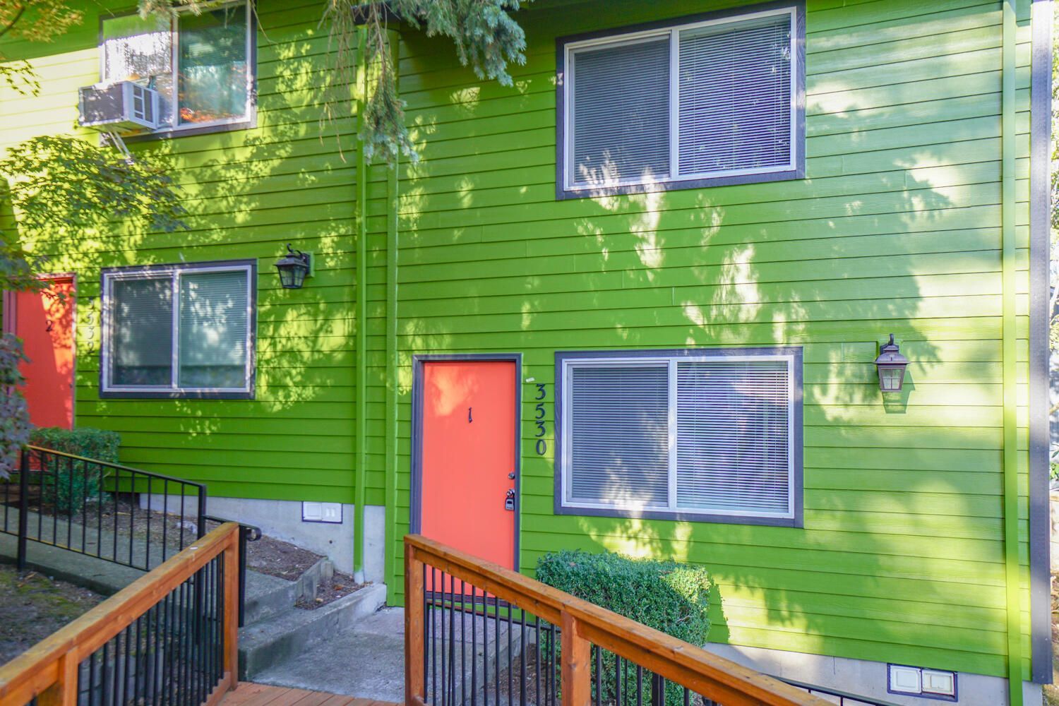 Green building with orange door, white windows, and wooden ramp.