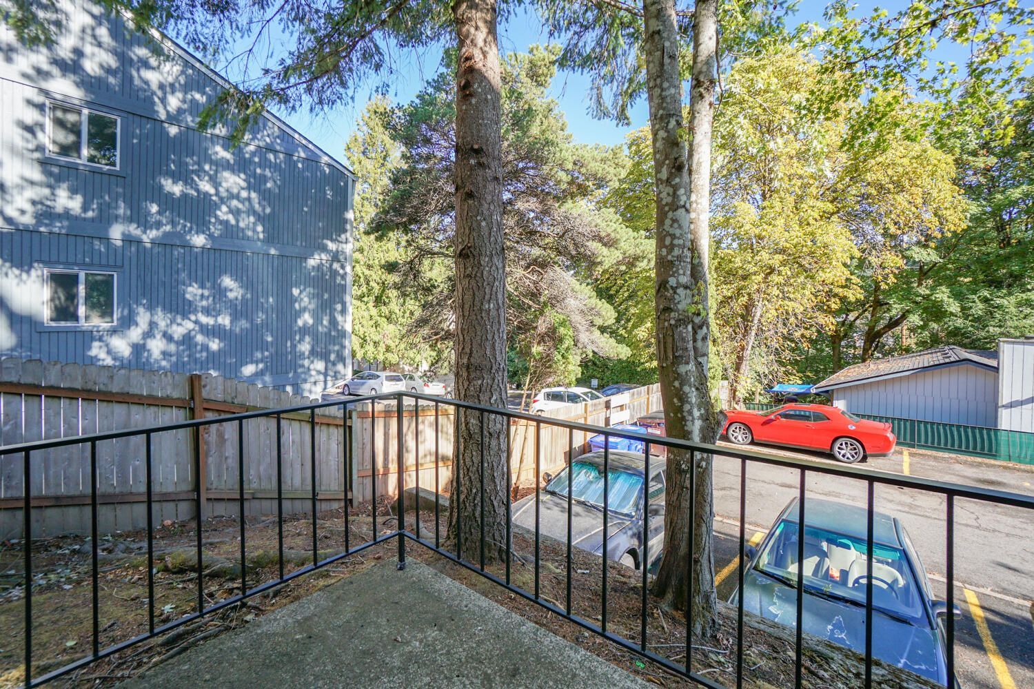 Balcony view: Apartment building, trees, parked cars, and metal railing.
