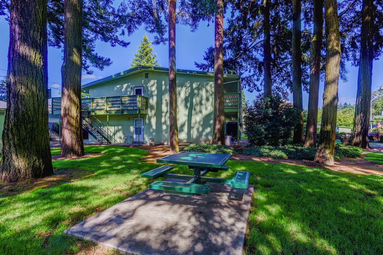 There is a picnic table in the middle of the woods in front of a house.