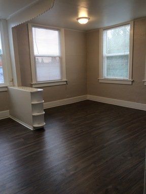 An empty living room with hardwood floors and two windows.