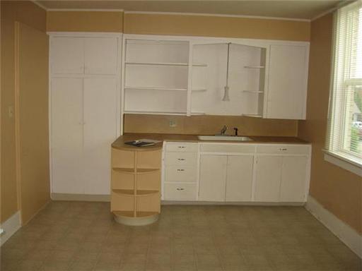 An empty kitchen with white cabinets and a sink.