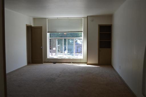 An empty living room with a large window and a carpeted floor.