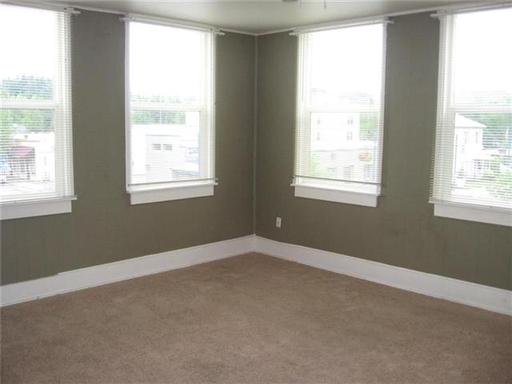 An empty room with three windows and a brown carpet.