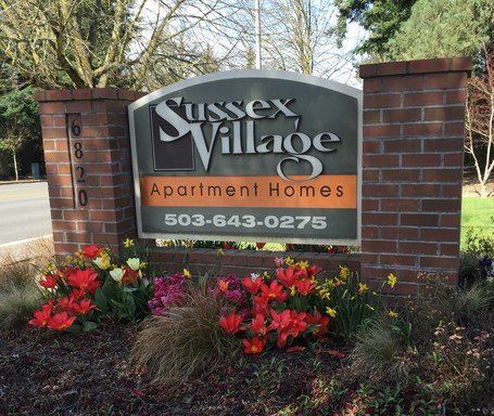 A sign for sussex village apartment homes is surrounded by flowers