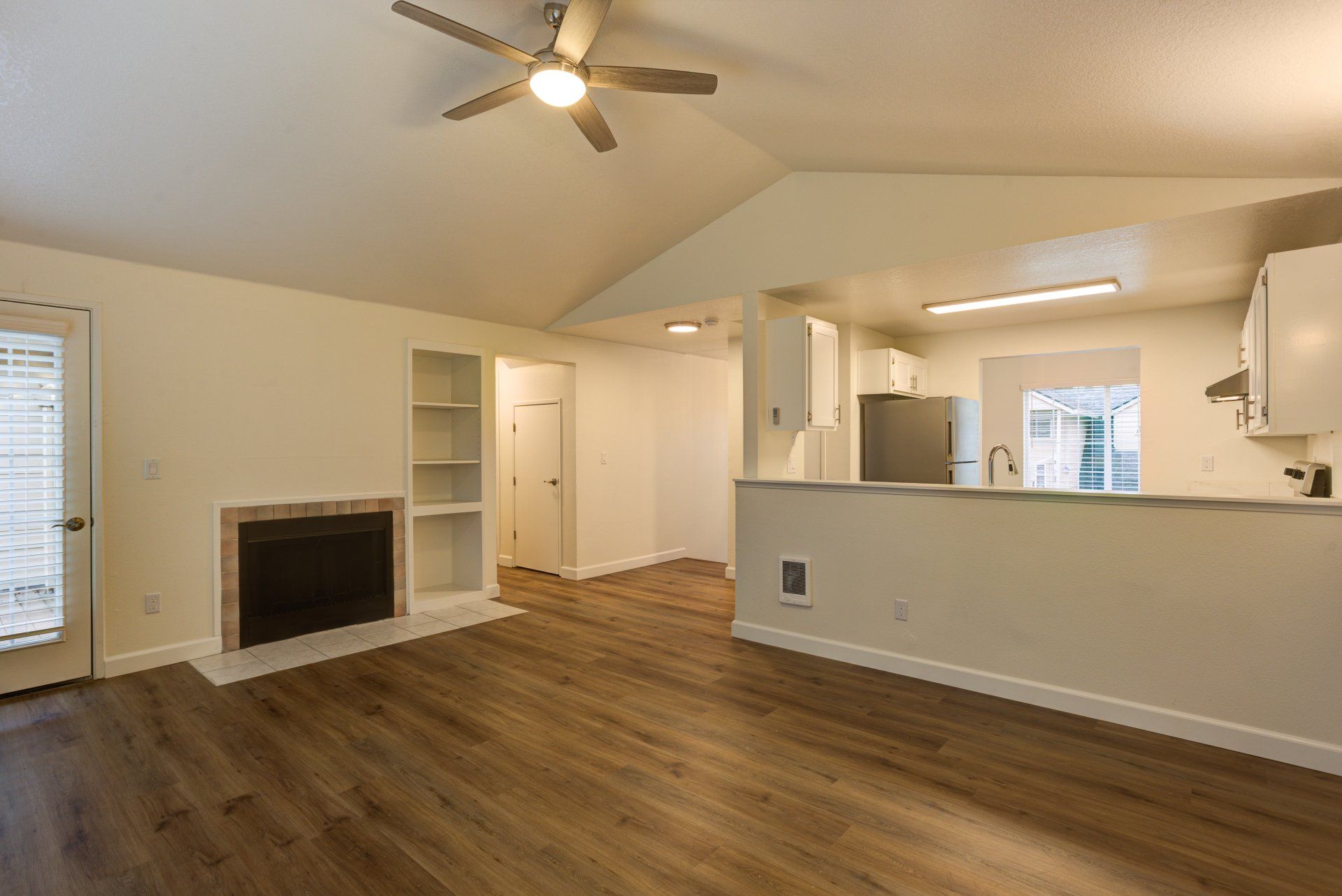 An empty living room with a fireplace and a ceiling fan.