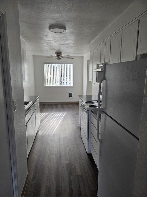 A kitchen with white cabinets , a refrigerator , a stove , and a window.