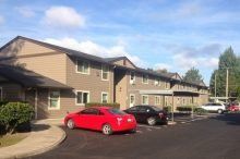 A red car is parked in front of a large apartment building.