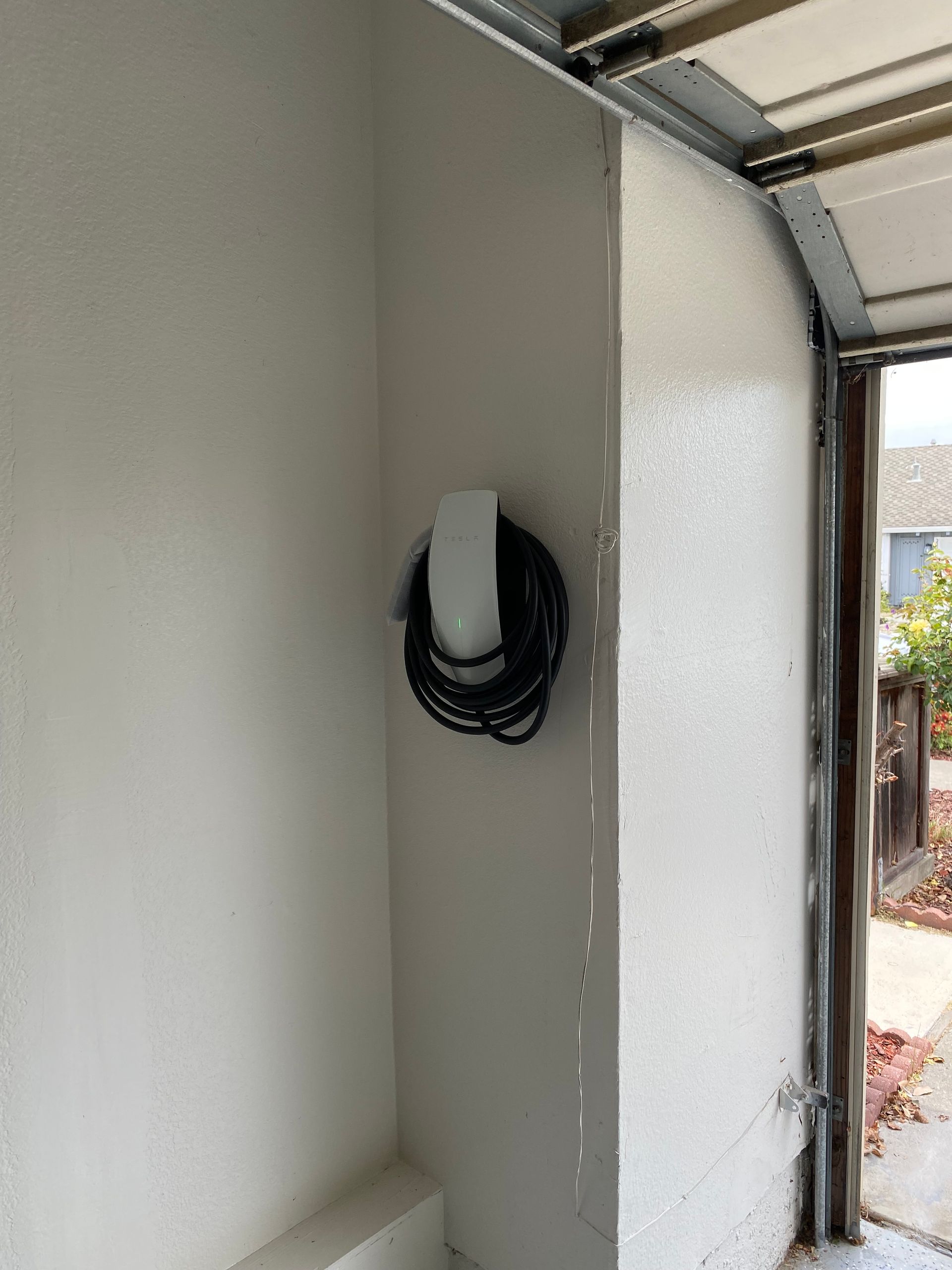 Open white electrical outlet cover on a garage wall near the door opening