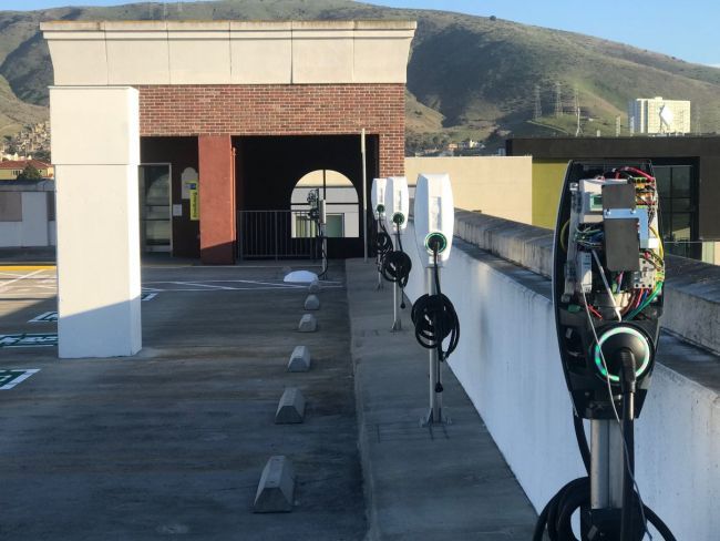 Parking garage rooftop with electric vehicle charging stations and distant hills in the background