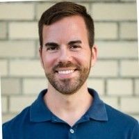A man with a beard is smiling in front of a brick wall.