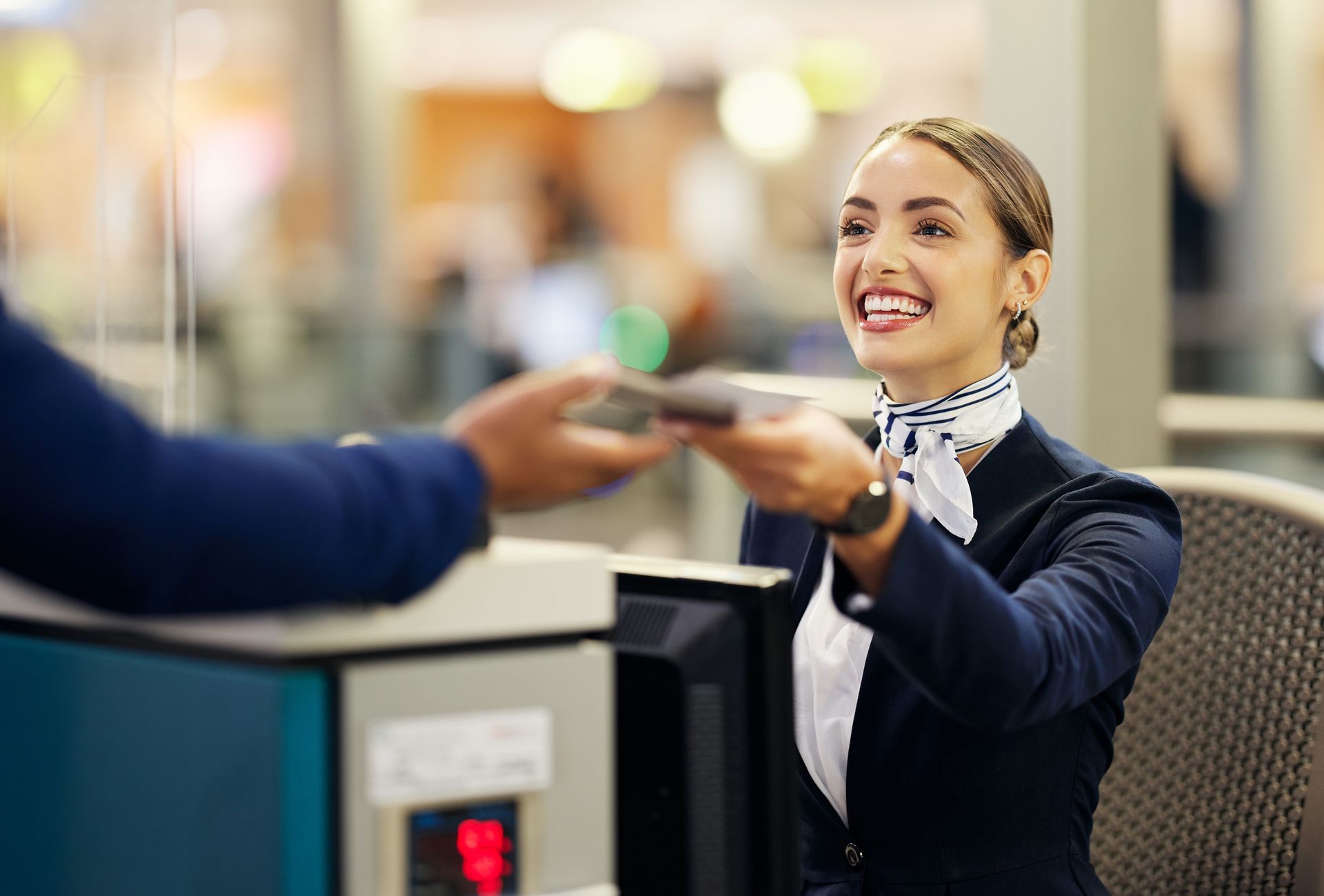 Female worker at an airport handing a traveler back his passport. 
