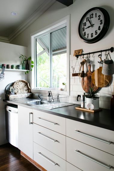 White kitchen with sink and counters, black clock, wooden cutting boards, and a window.