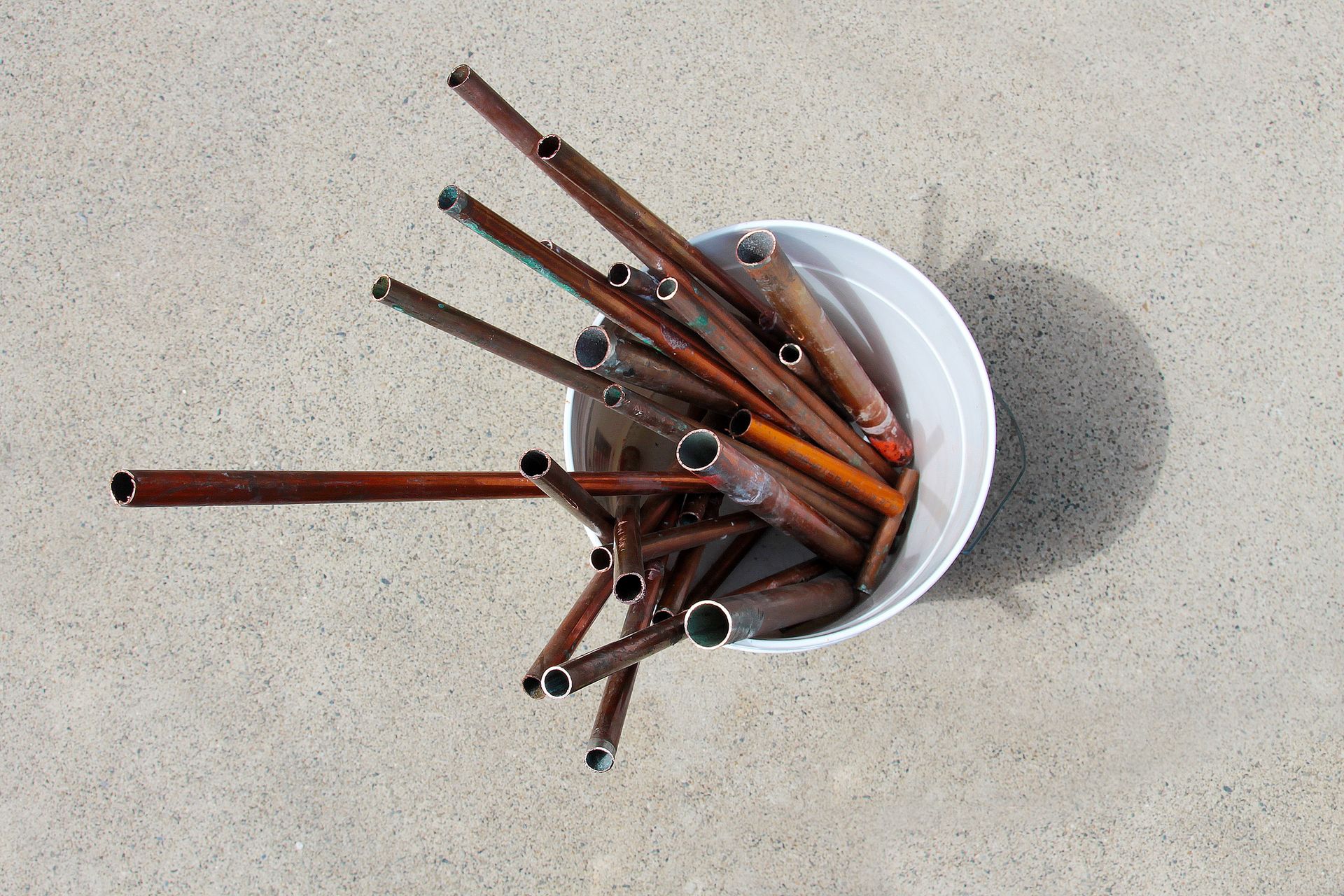 A White Bucket Filled With Copper-colored Metal Tubes on a Concrete Surface — B & B Scrap Metal in Maroochydore, QLD