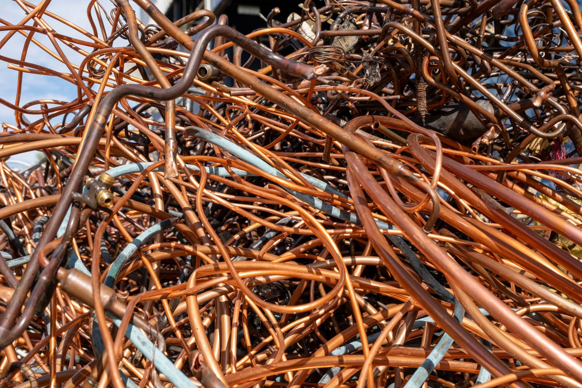 Tangled pile of copper tubing, varying in shades of brown and copper, outdoors.