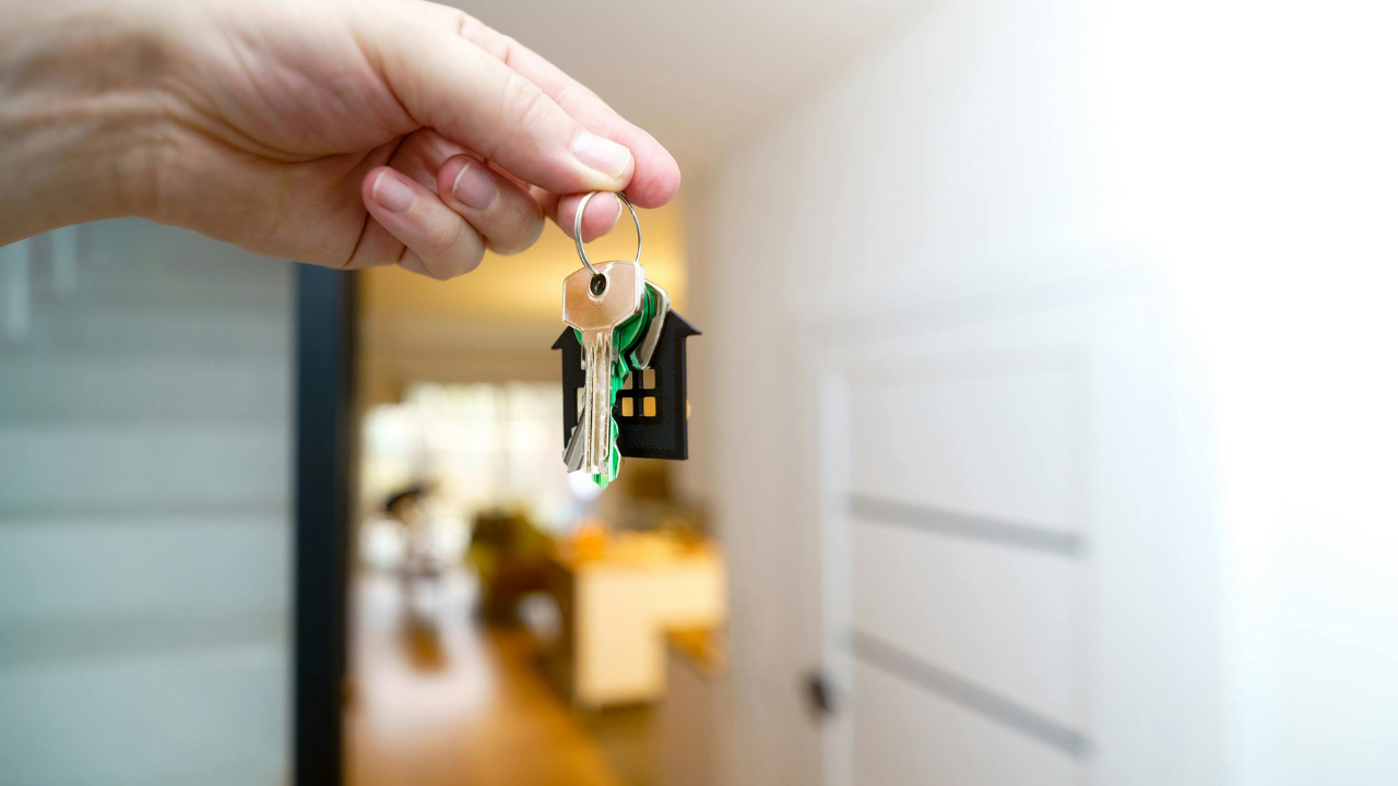 Smiling man in suit holding cardboard house and keys.