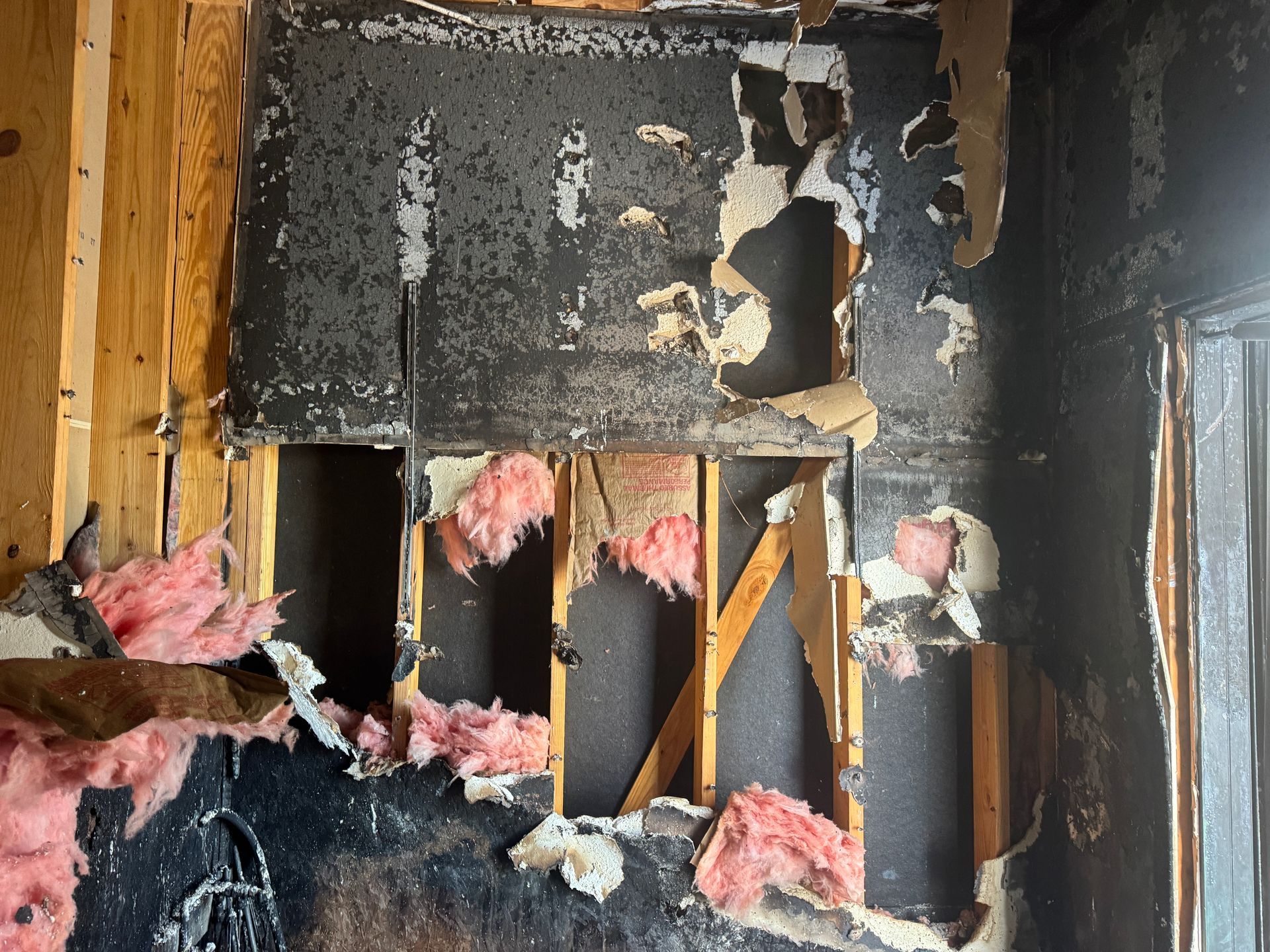 Interior wall damaged by fire; charred wood, exposed insulation, and peeling paint.