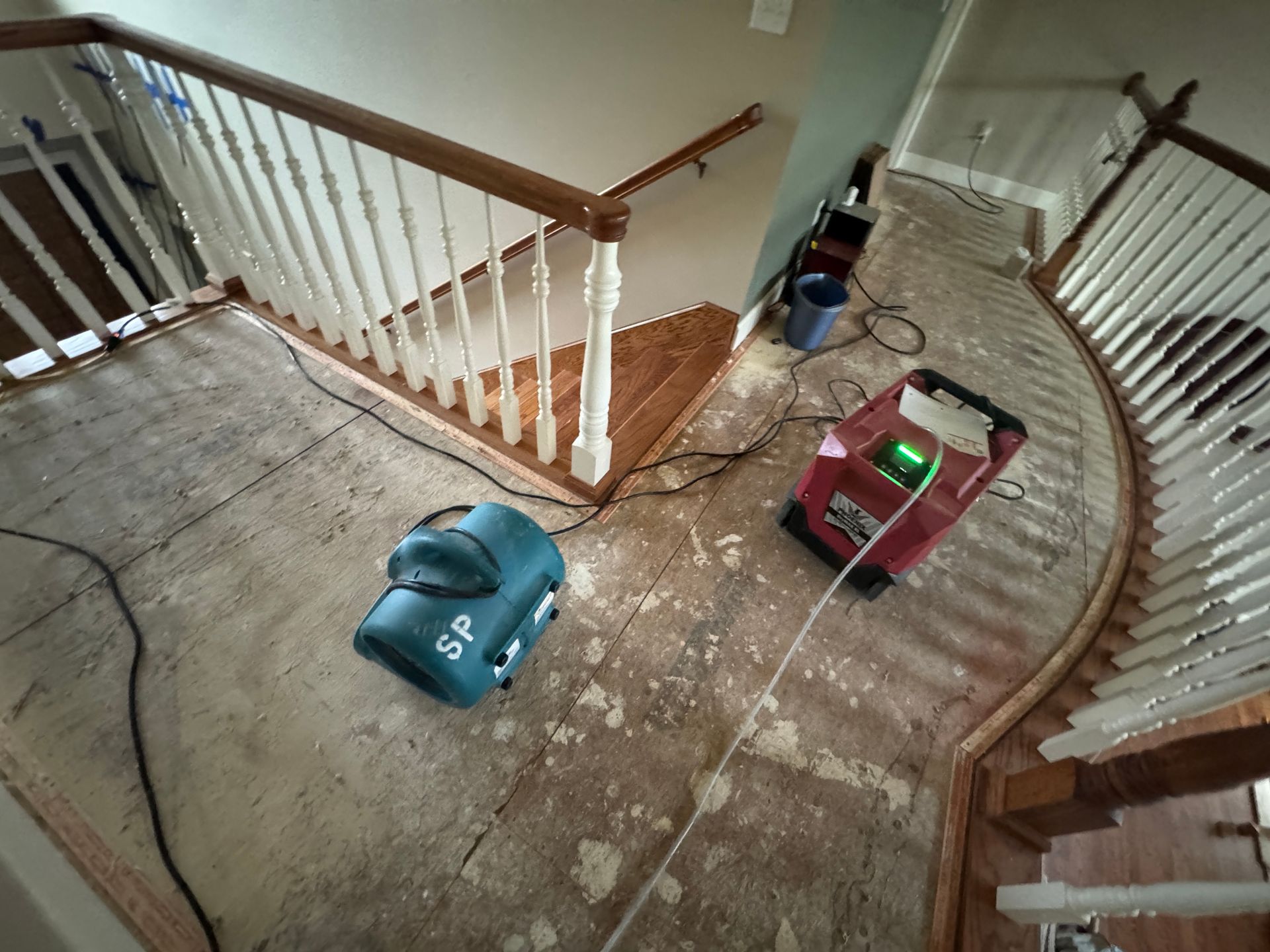 Two water damage restoration machines drying carpet remnants on a landing next to a staircase.