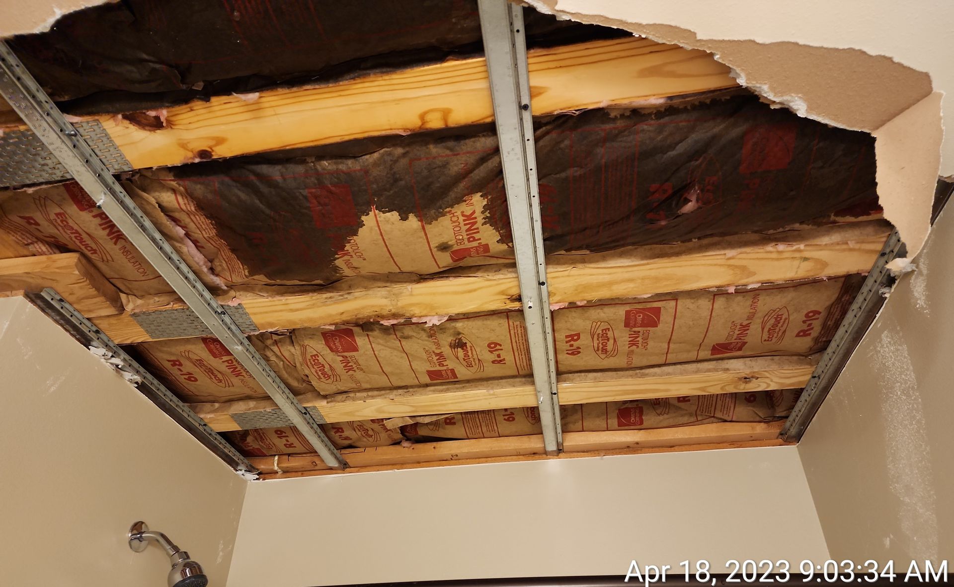 A damaged ceiling with exposed wood beams, insulation, and metal supports. A large section of drywall is torn away.