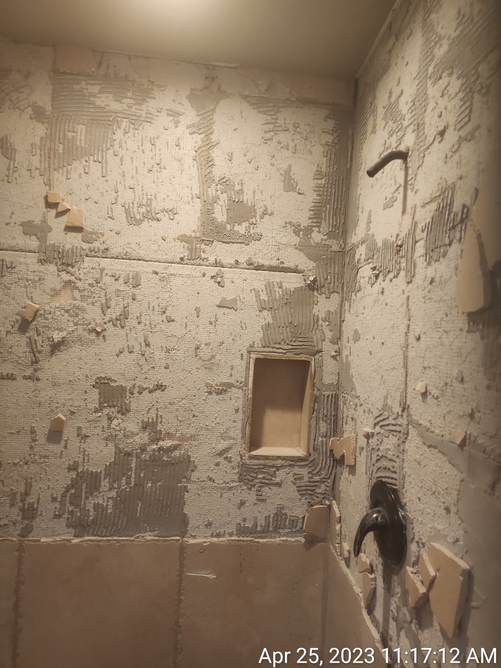 Bathroom interior showing damaged walls, a showerhead, and a built-in shelf. 