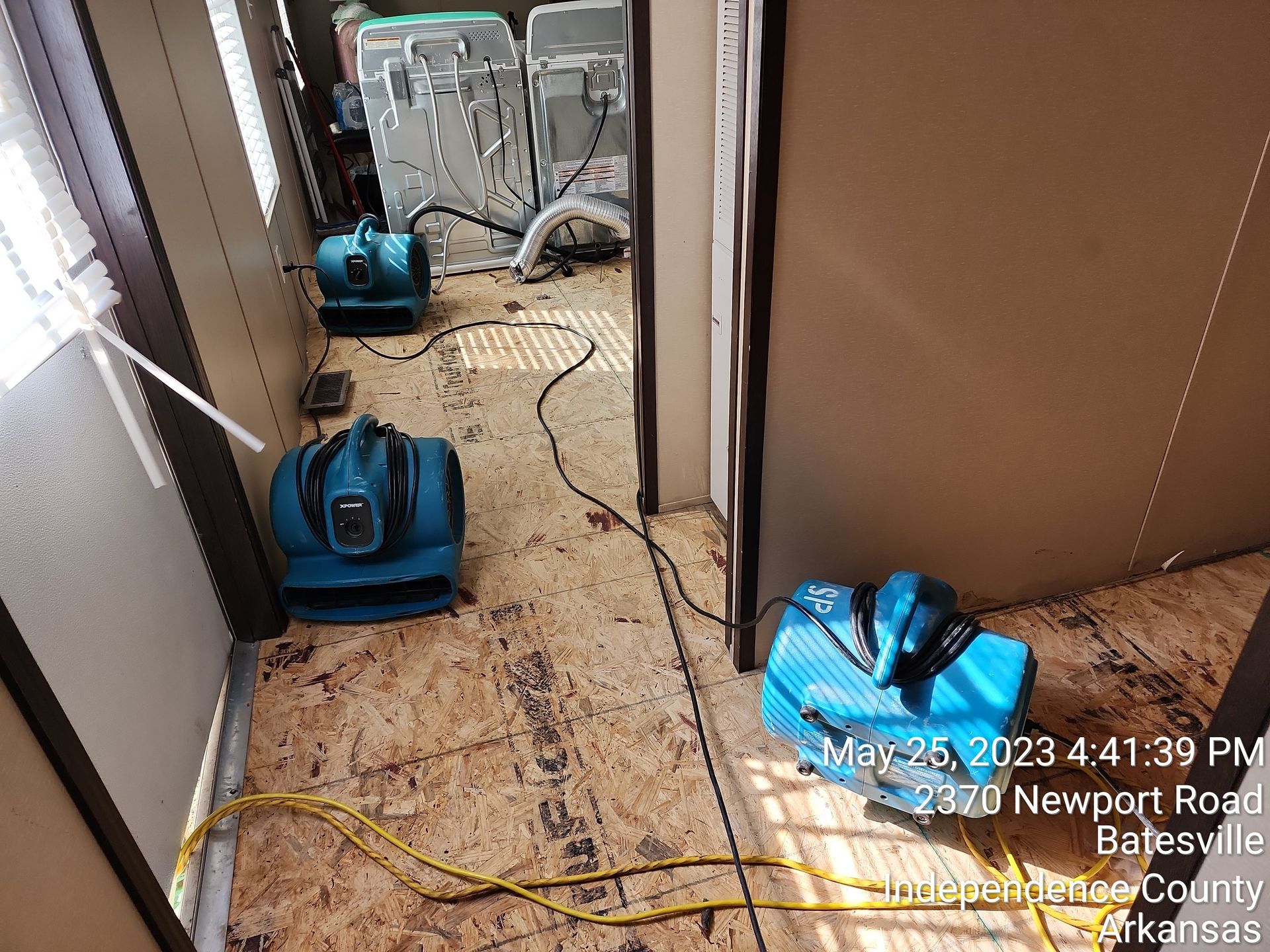 Three blue fans on a floor, likely drying it after a flood. Setting is an indoor room with other drying equipment visible.