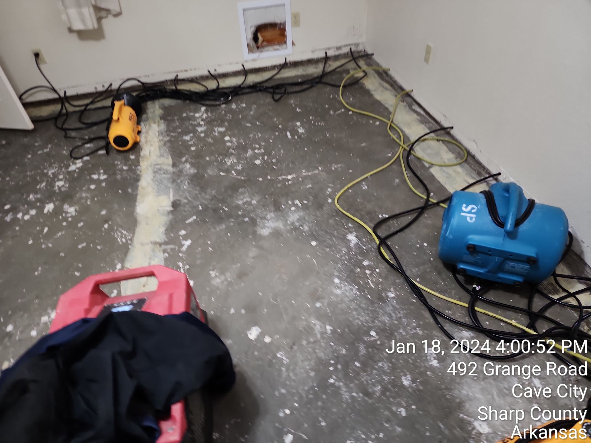 Dehumidification equipment in a room with exposed concrete floor. Date and address in the bottom right.