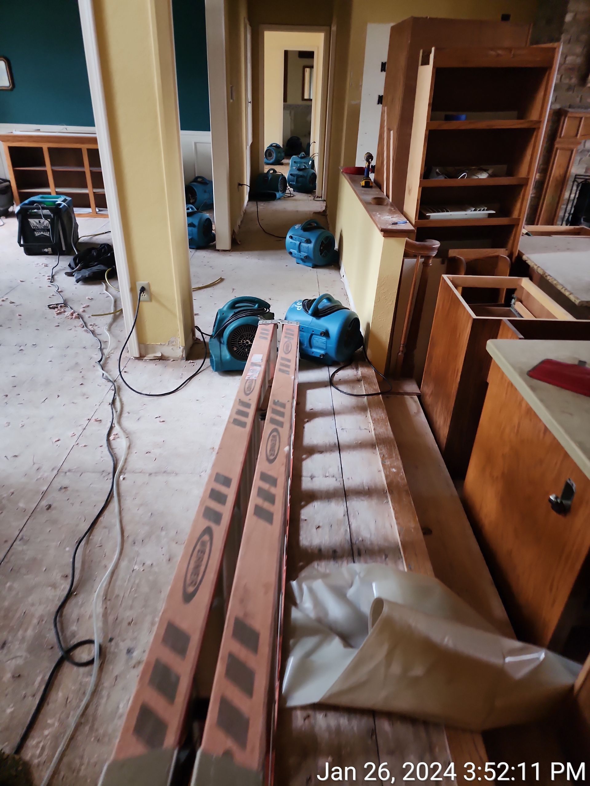 Dehumidifiers and equipment are in a hallway and kitchen area, indicating water damage restoration. 