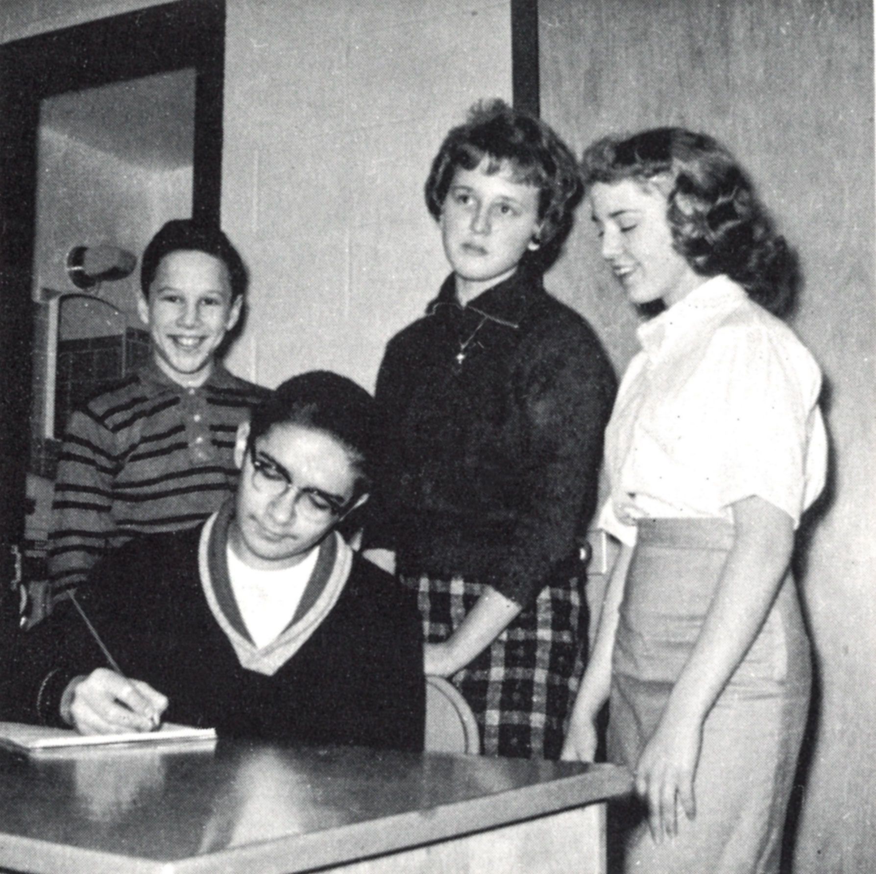 Two make and two female students, one male is seated at a desk writing.