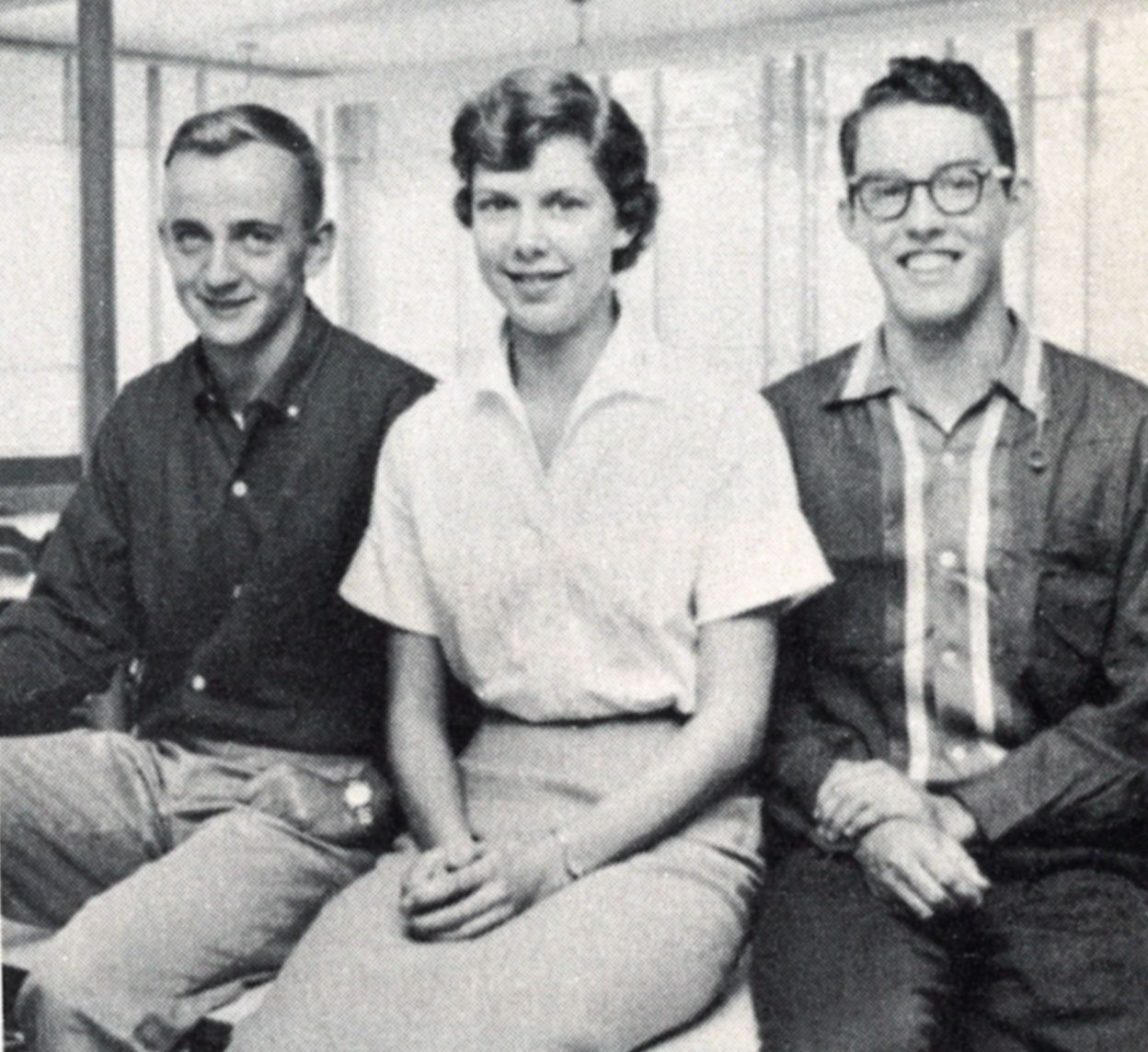 Three smiling, sitting students--two guys with a girl between them.
