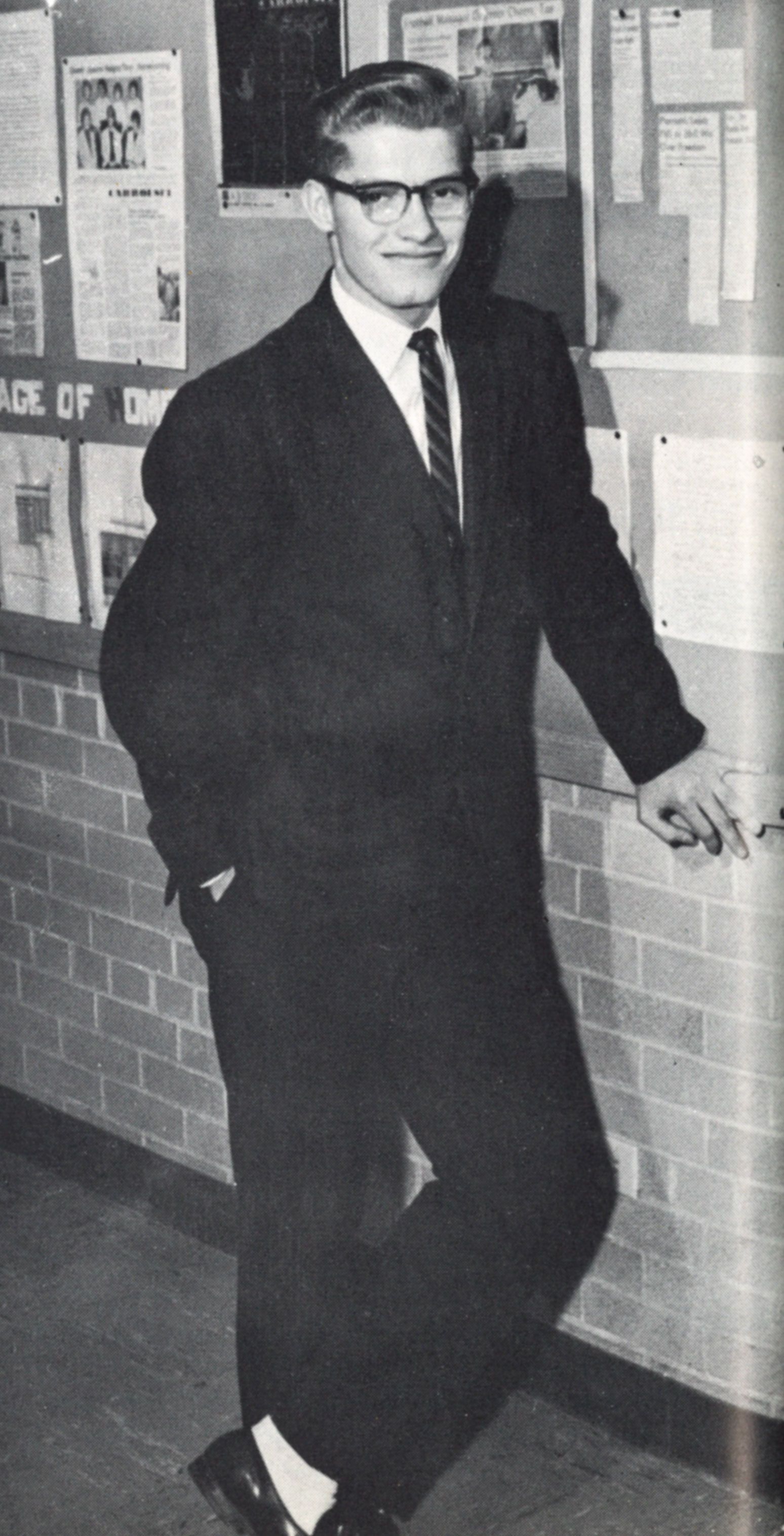 Student in a suite and tie, standing by a bulletin board