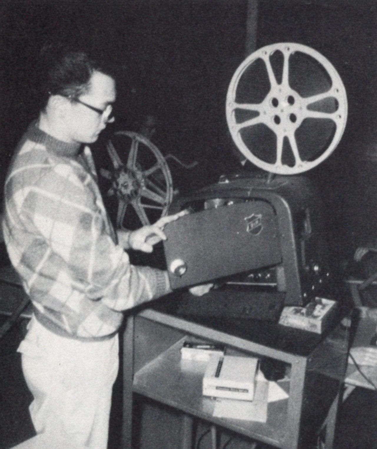 Student by a film projector, with the side door of the projector open.