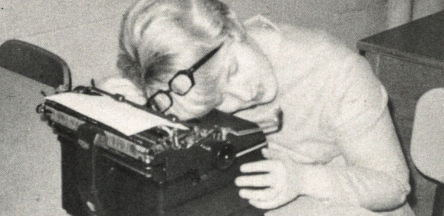 Female student with glasses on her head, her head on a typewriter, and her eyes closed.