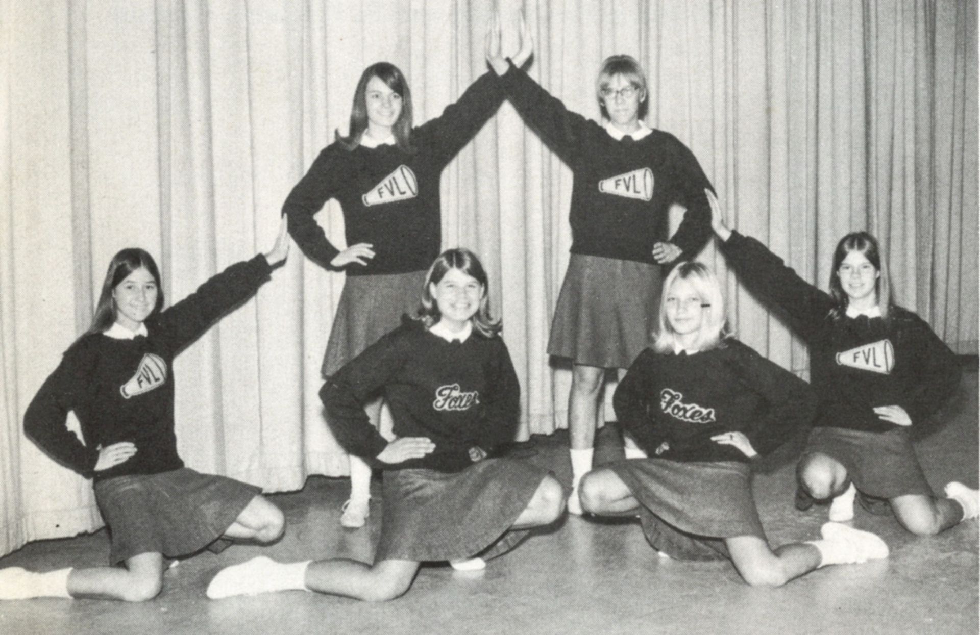 6 cheerleaders in uniform, striking a pose for the camera and smiling