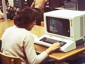 Female student sitting at a table, working on a computer from the 1980s