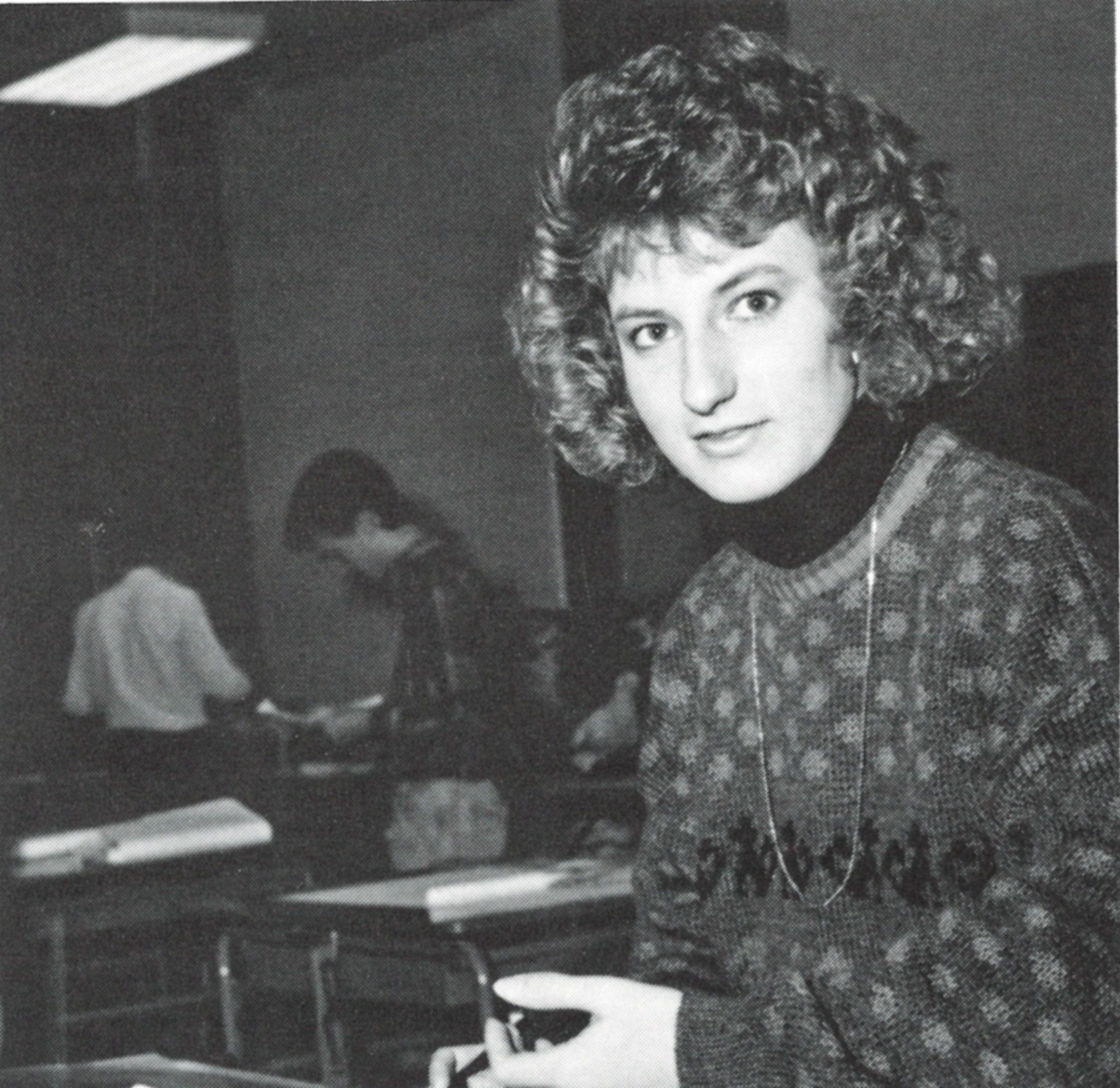 Female student at a desk, holding a pen, and looking at the camera