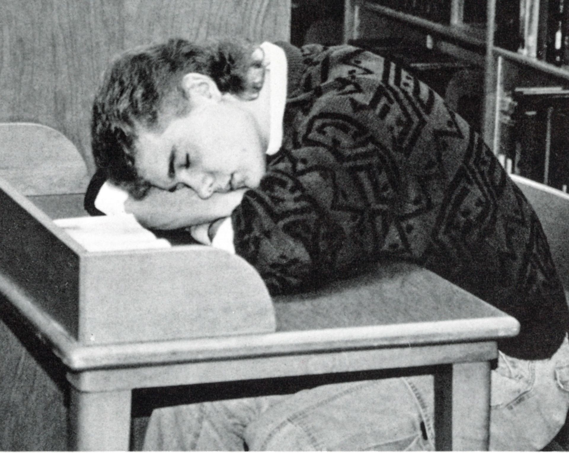 Male student with his head on his crossed arms on a desk, and with his eyes closed