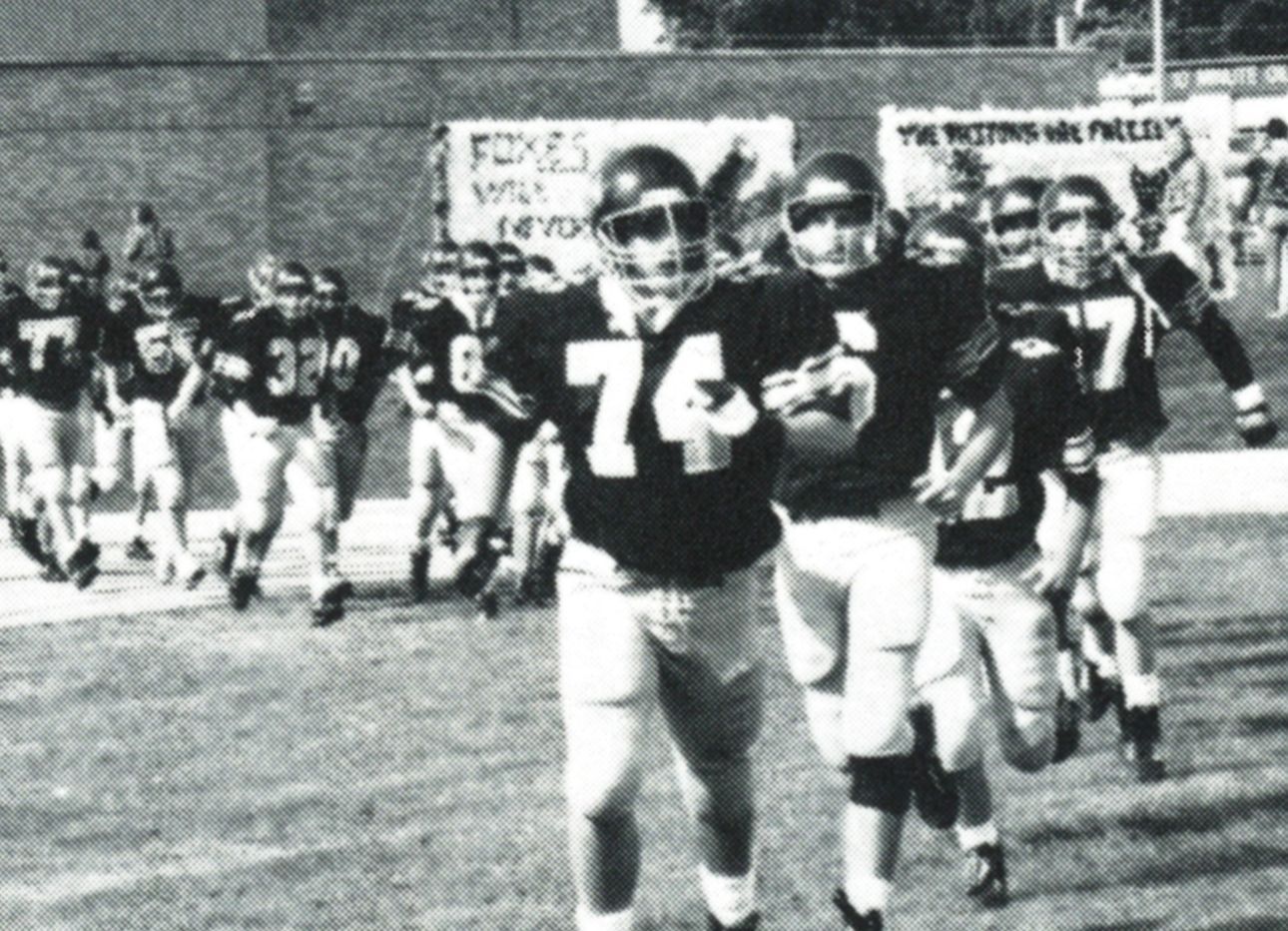Line of football players in their gear, running onto the field