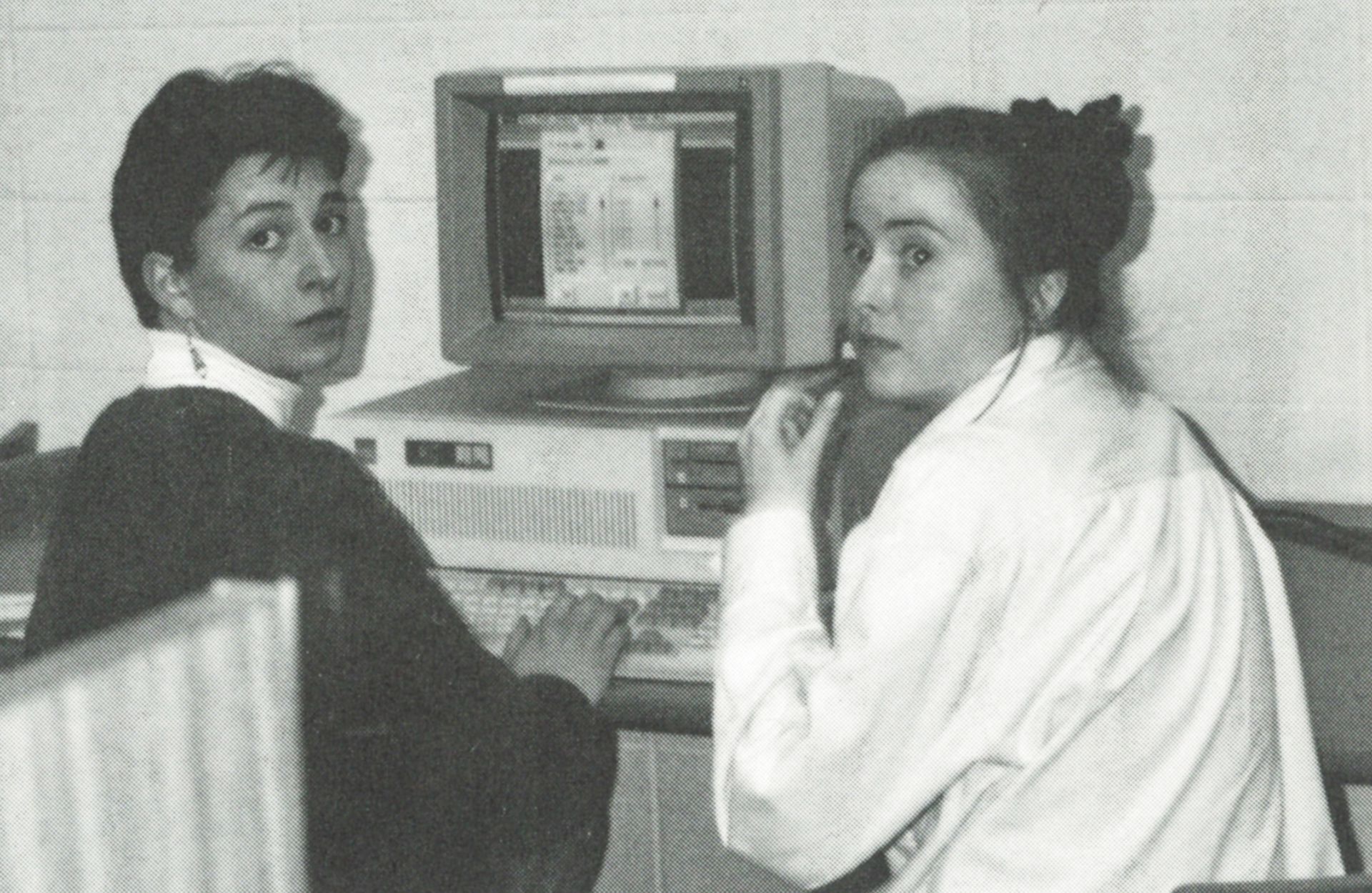 Two girls at a computer, turned around to look toward the camera