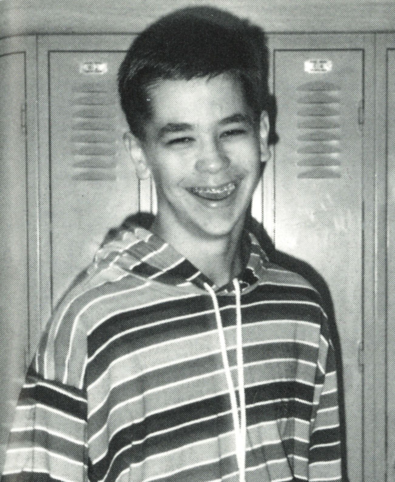 Happy boy standing by lockers and wearing a striped hoodie tshirt