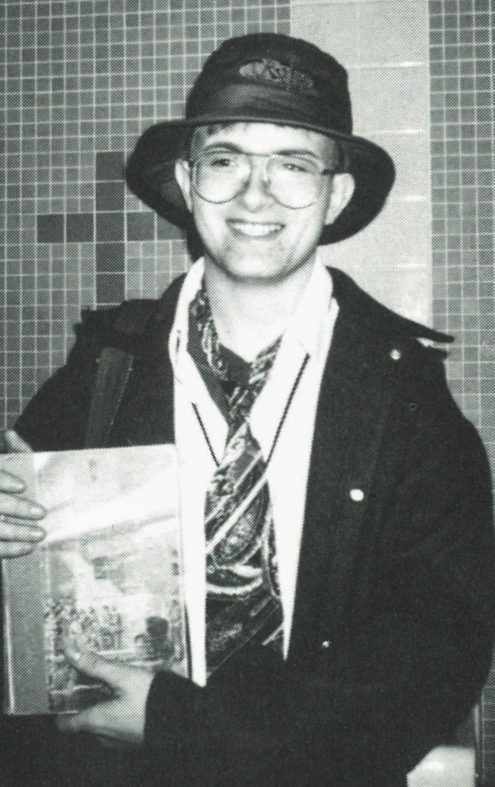 Smiling male student with glasses, wearing a hat and loose tie