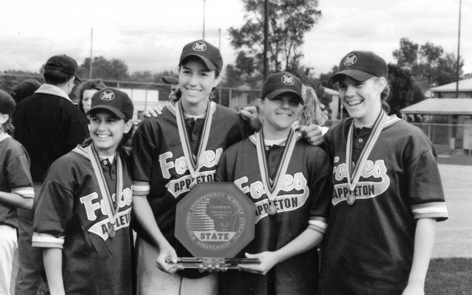Four members of the 1998 state championship softball team, wearing their medals and holding the trophy