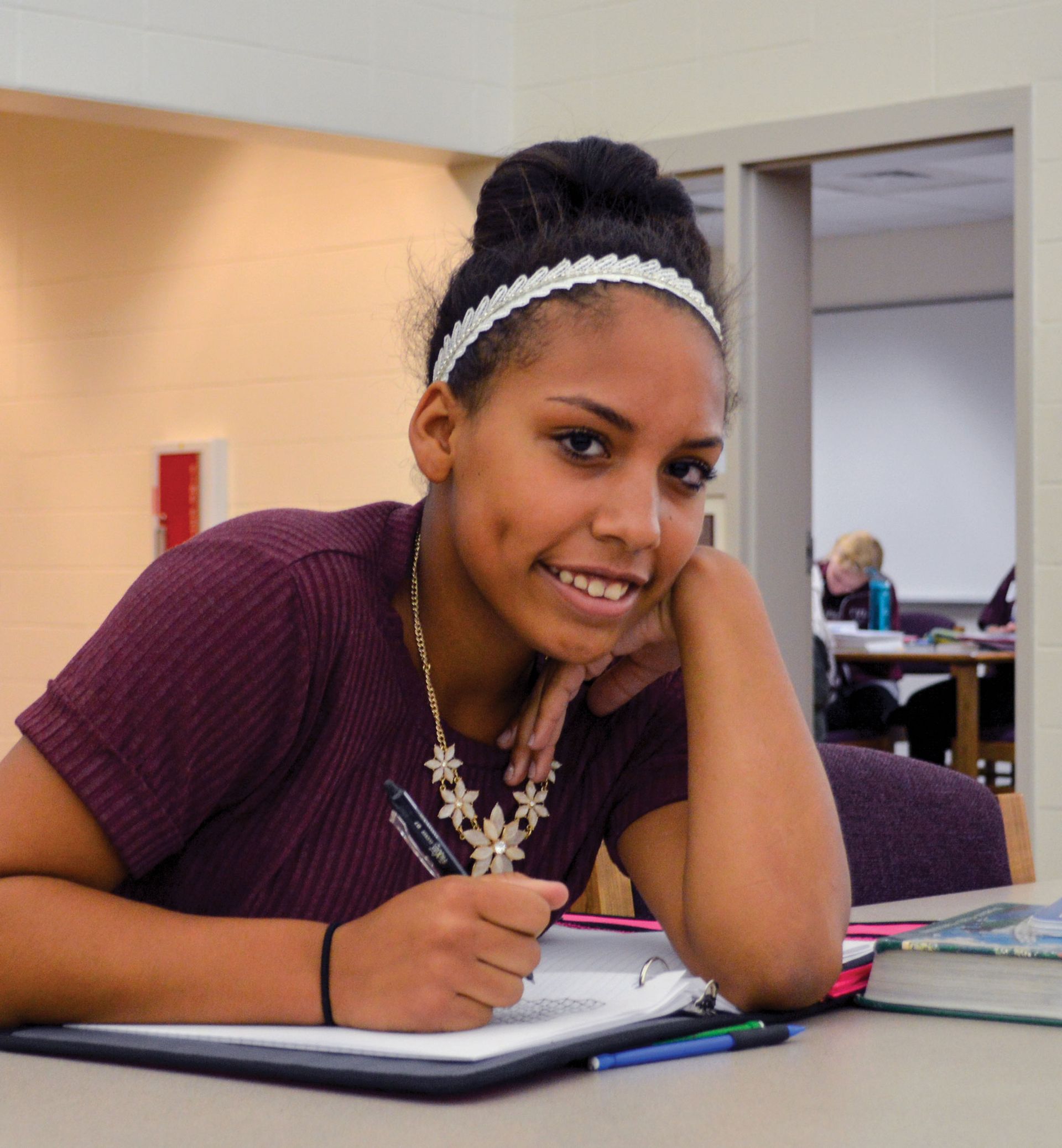 Smiling girl looking at the camera with school work on the table in front of her