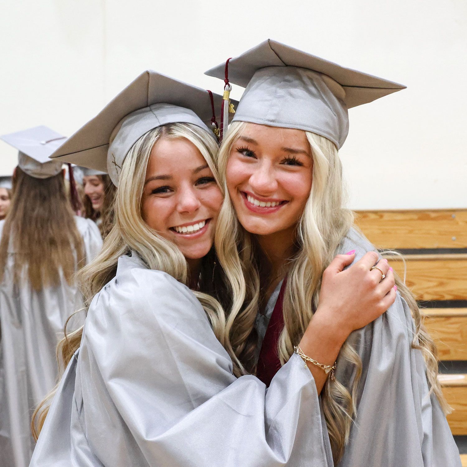 Two smiling female students hugging, and in small gym prior to service