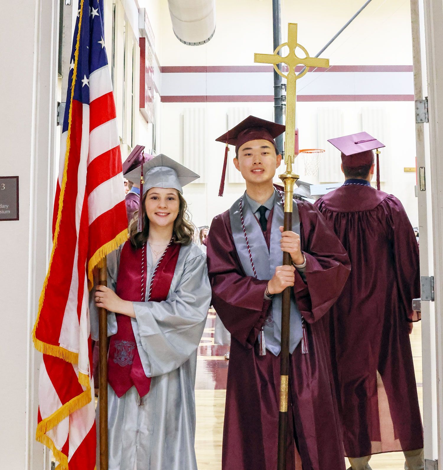Smiling female student holding US flag, smiling male student holding cross, prior to service