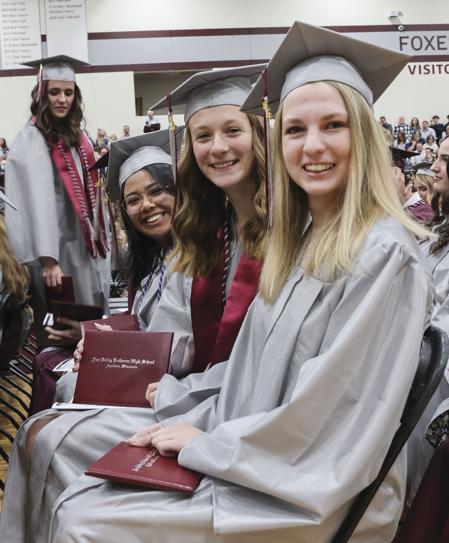 Three smiling females, in chairs, after receiving diplomas