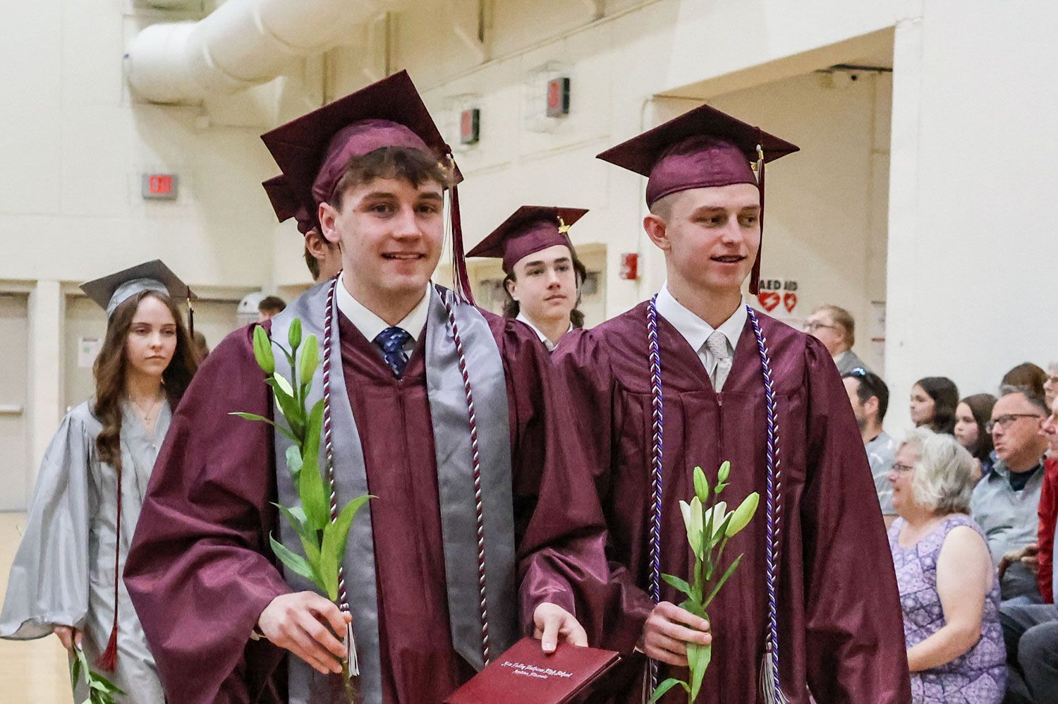 Male students in recessional, holding flowers and diplomas